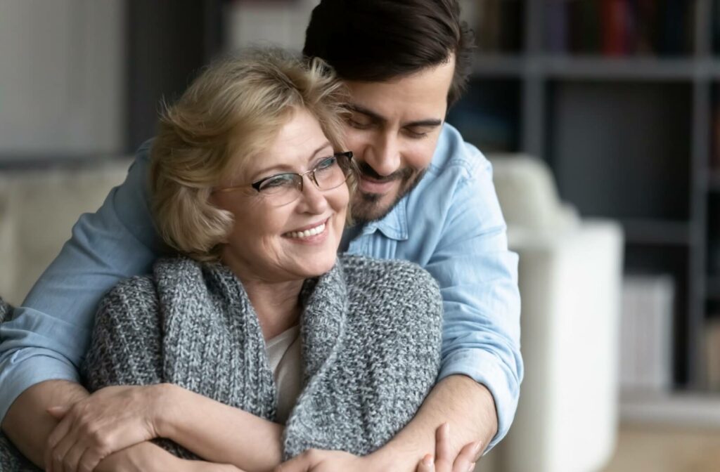 A senior and their older adult child hugging and smiling in a living room