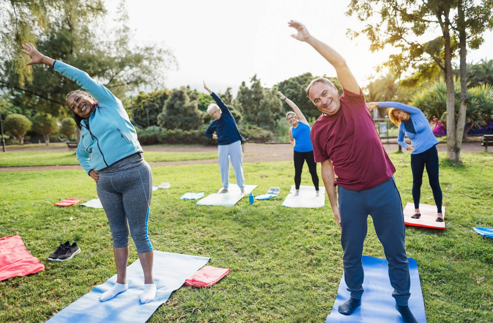 A group of senior adults standing on a yoga mat doing exercise in a park