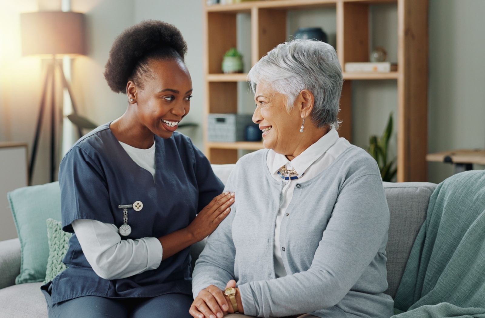 A smiling staff member and older adult sitting on a couch in personal care.