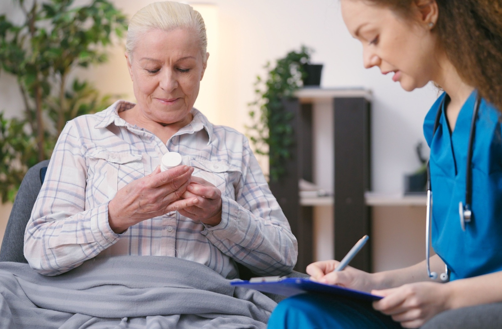 A staff member writing on a clip board while going over medication with an older adult holding a pill bottle.
