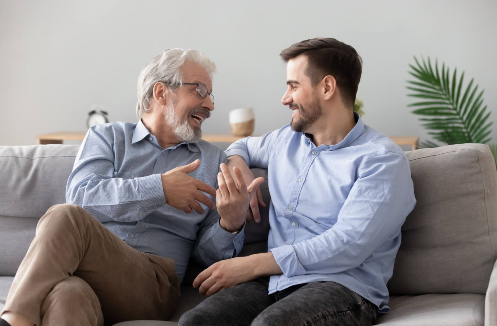 An older adult in assisted living talking with their adult child on the couch and laughing during a visit.