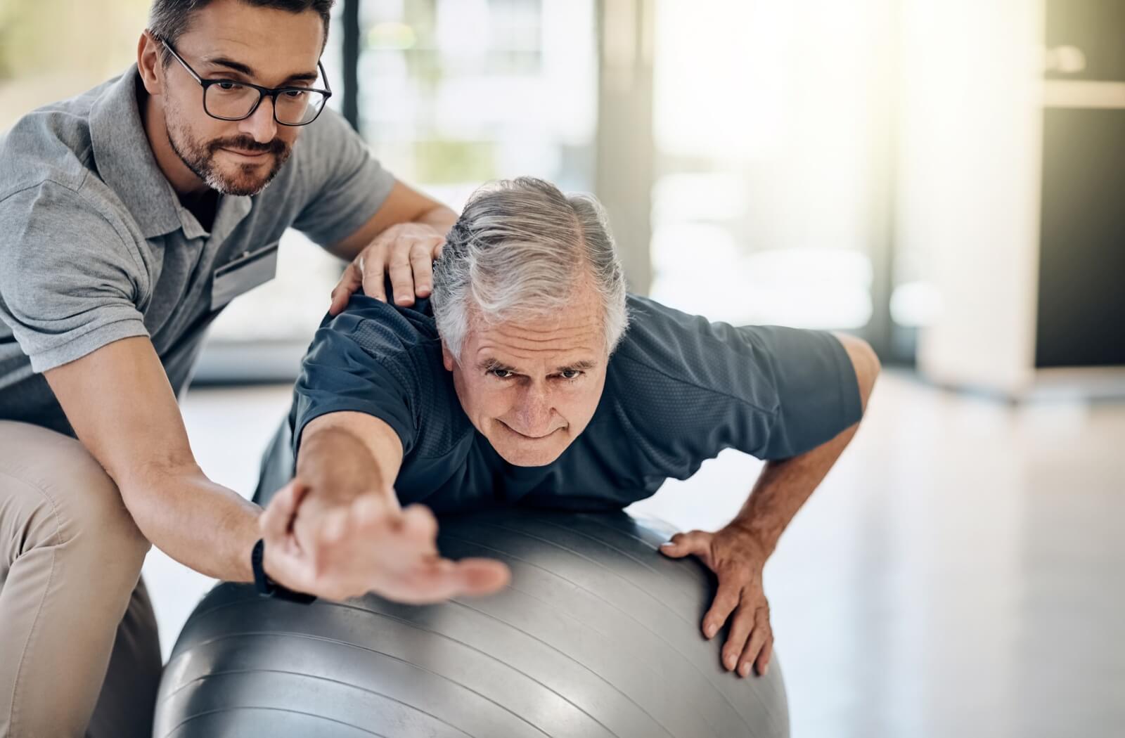 A physiotherapist assists a senior with shoulder mobility exercises on an exercise ball.