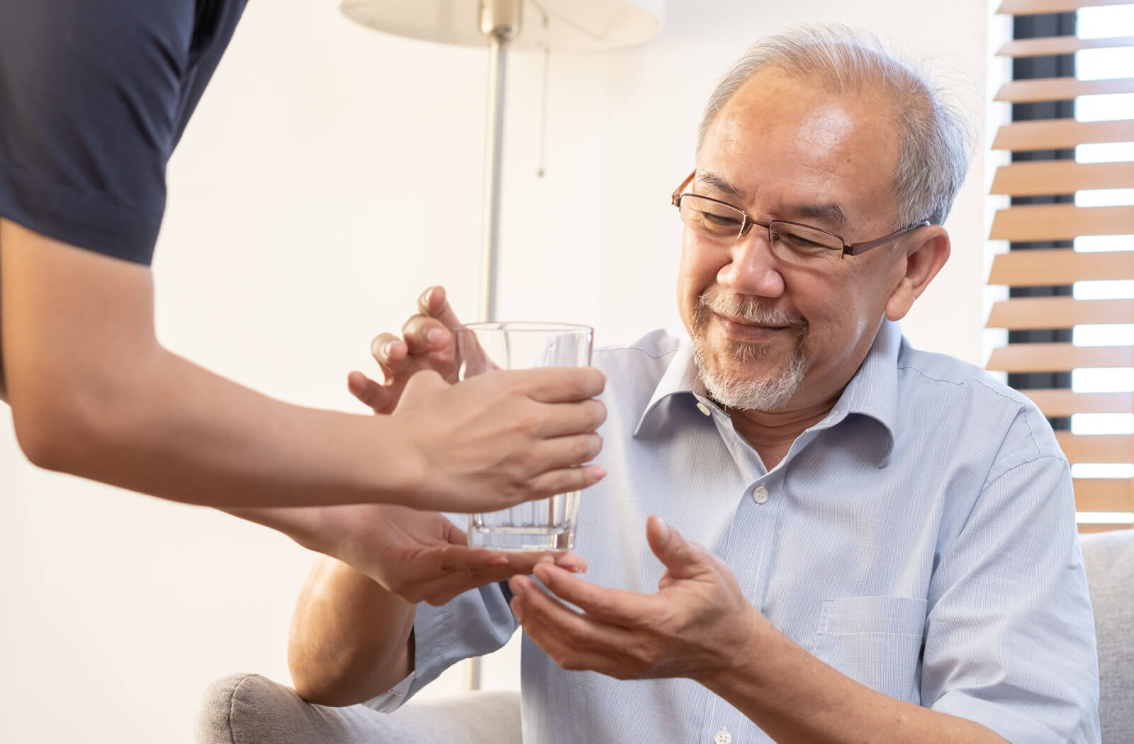 A caregiver handing an older adult with dementia a glass of water to help them stay hydrated.