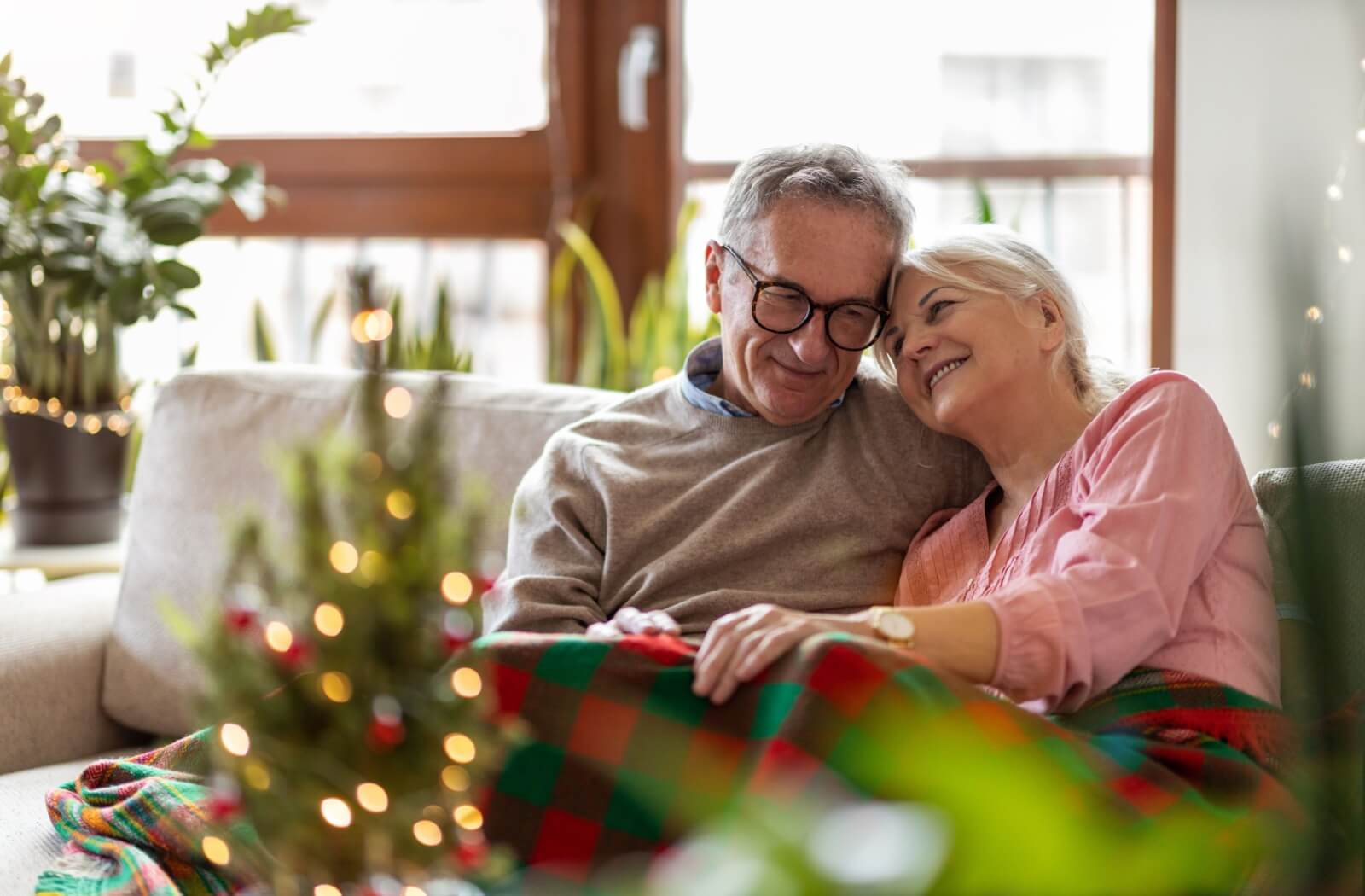 A happy senior couple cozy up with each other underneath a warm blanket on a cool winter day.