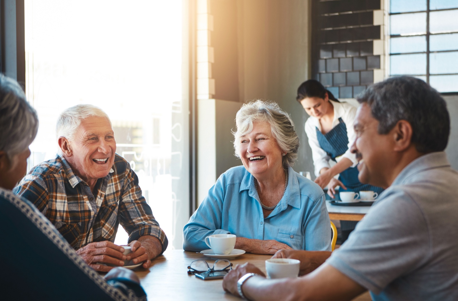 A group of older friends laughing in a sunlit cafe while bonding over coffee.