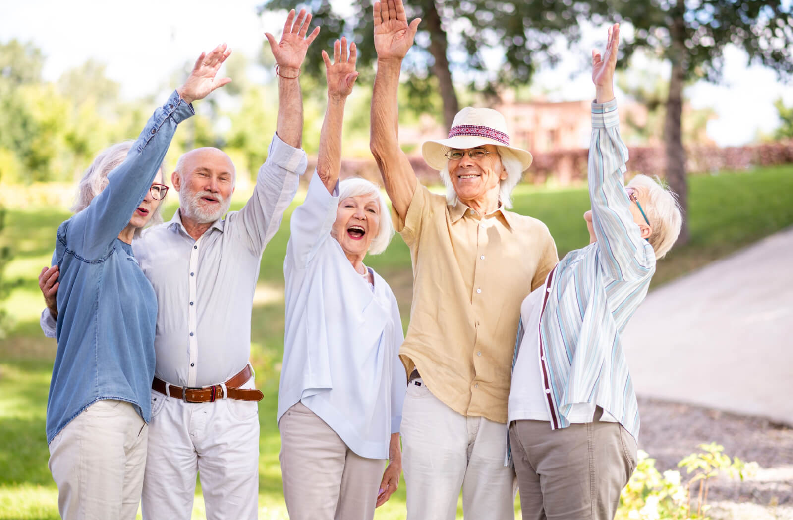 A group of 5 older friends outside with their hands in the air, laughing and celebrating.