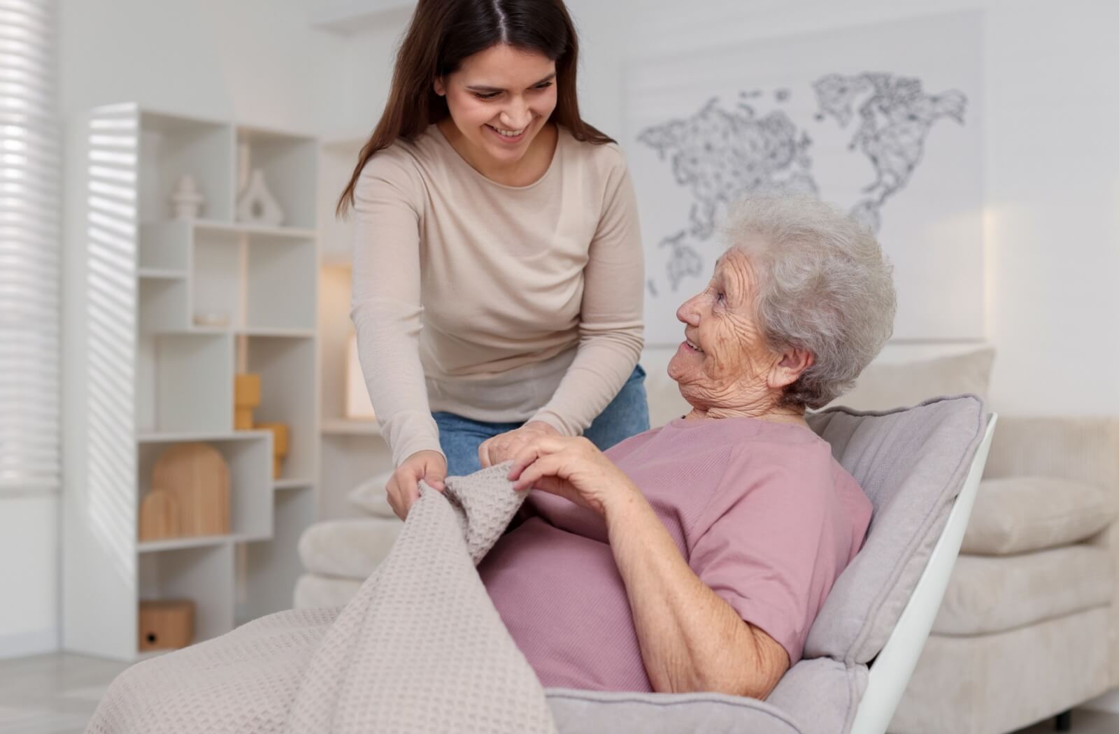 Caregiver helping senior with blanket in comfortable personal care setting with soft lighting and homey decor
