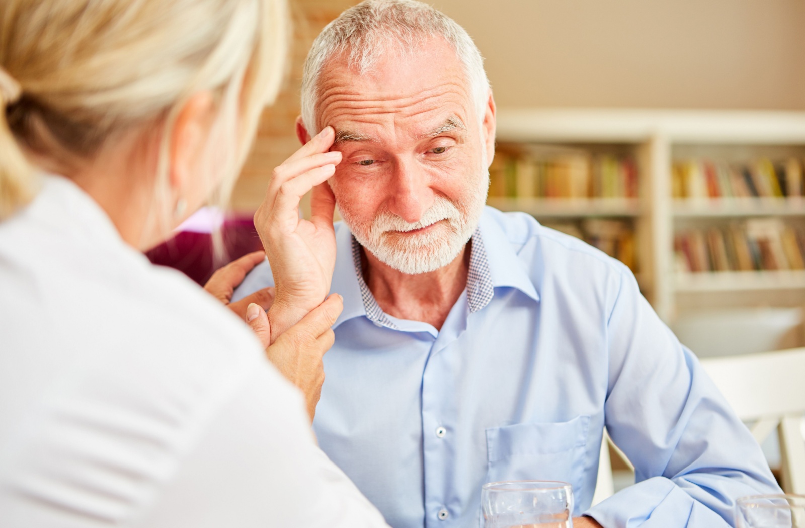 An older adults touches their temple during a healthcare checkup with a doctor to discuss their stress levels
