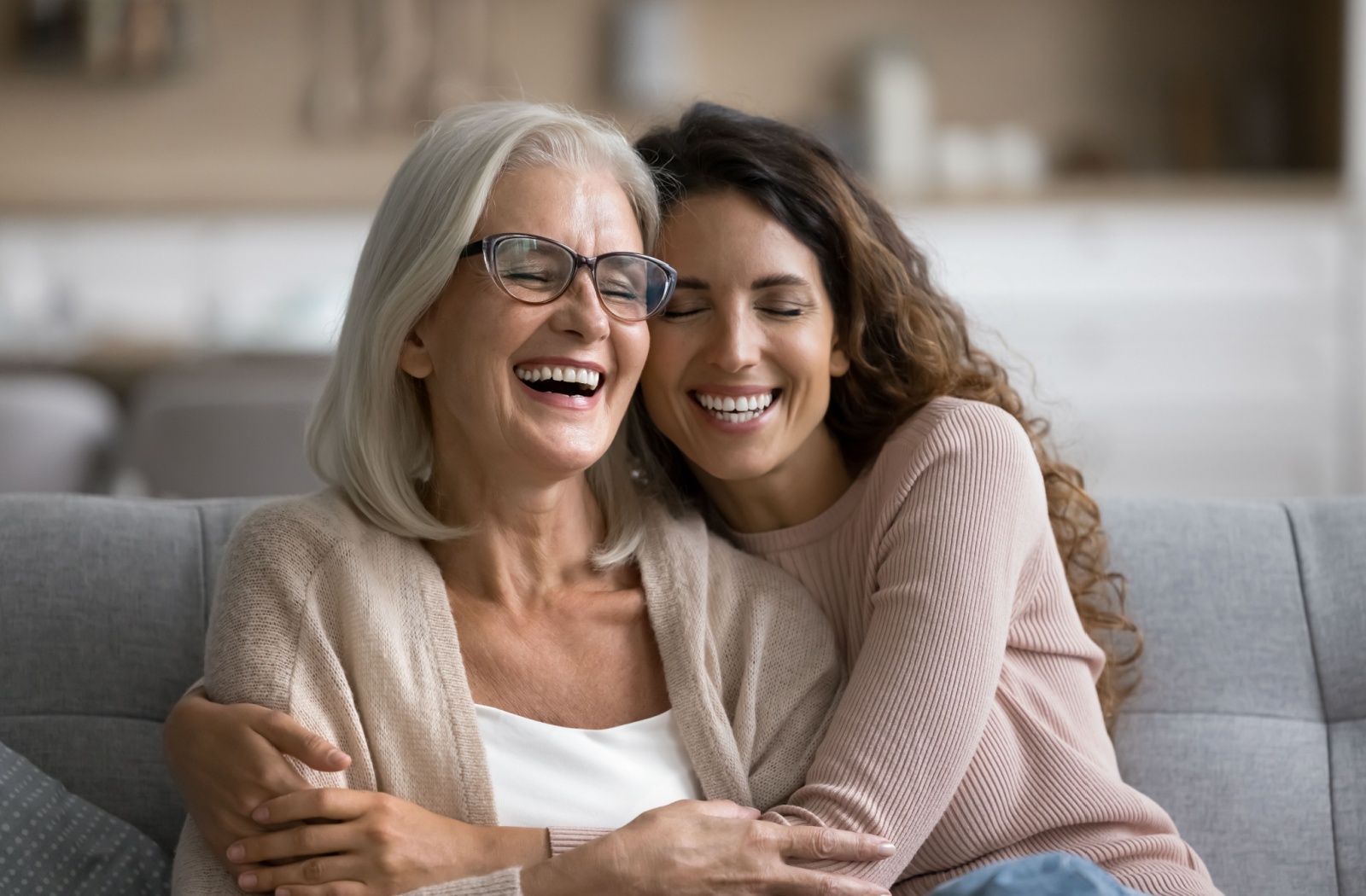 An adult child laughs and embraces their senior parent in a personal care community.